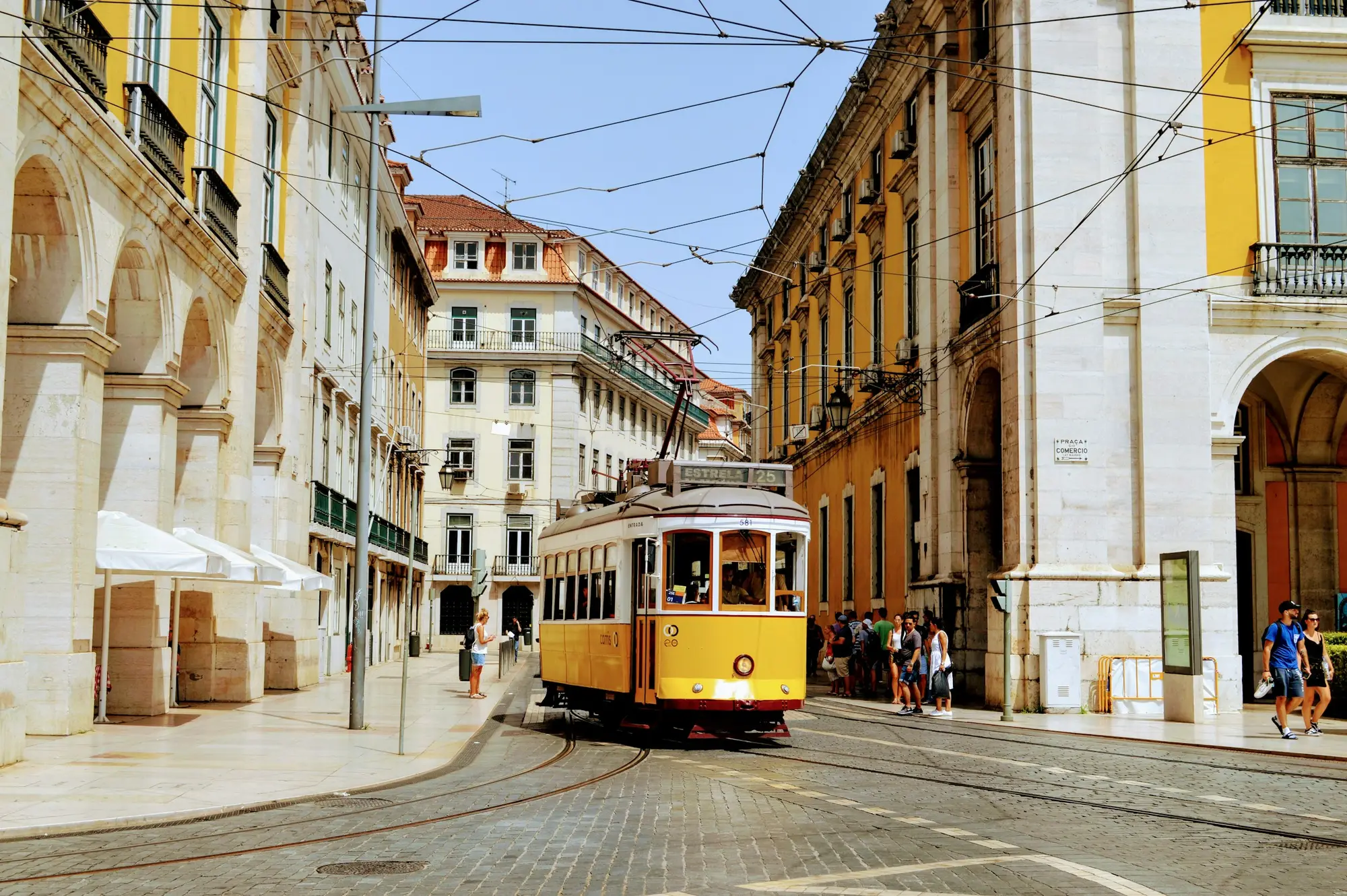 A yellow vintage tram on a cobbled Lisbon street lined with grand pale buildings