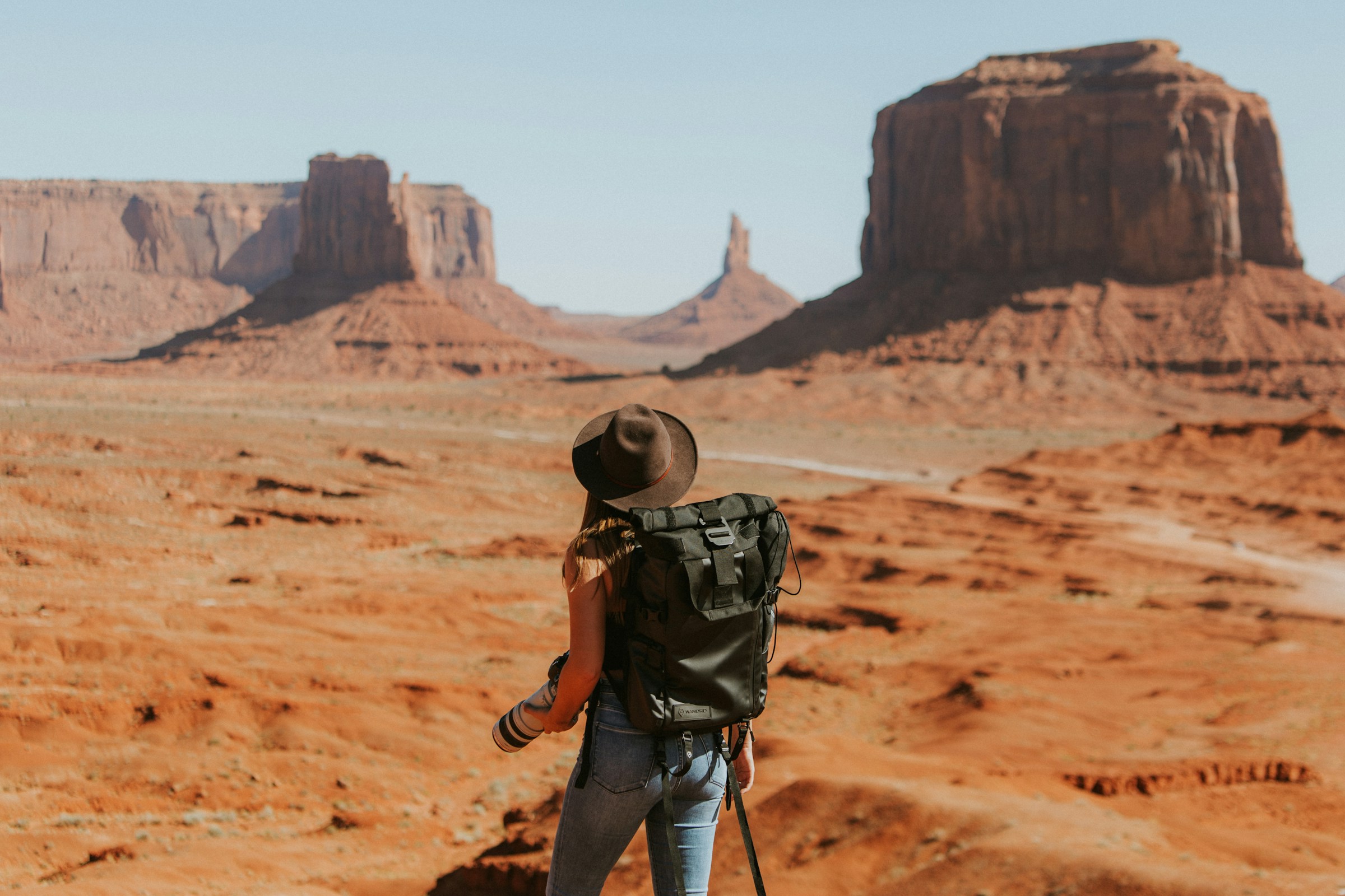 Woman with a black backpack standing alone in a wide open landscape, viewed from behind