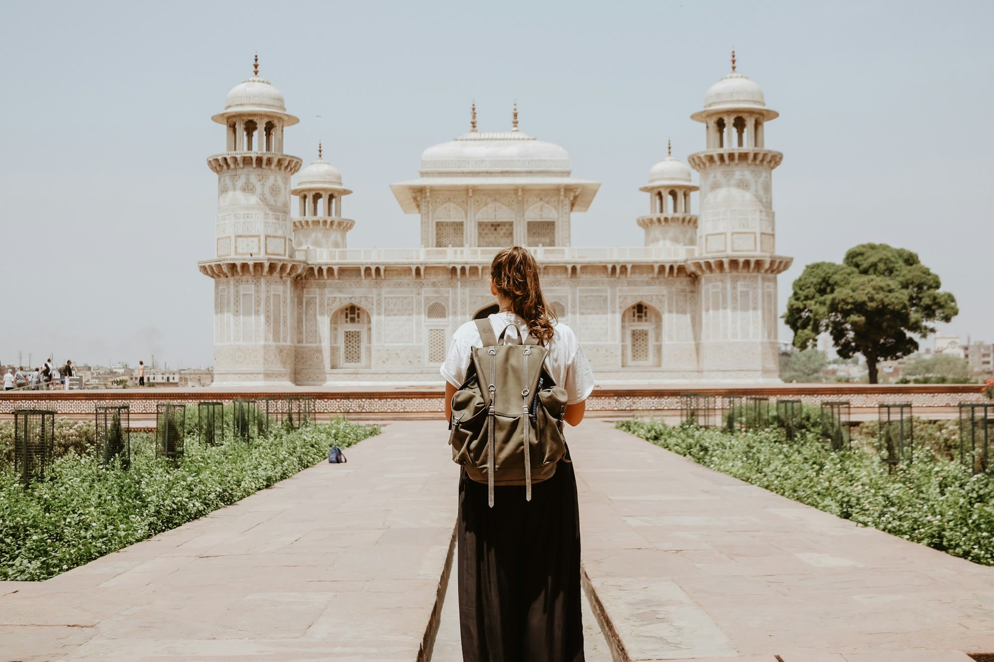 Woman with a backpack seen from behind, standing alone at a world heritage monument while traveling solo