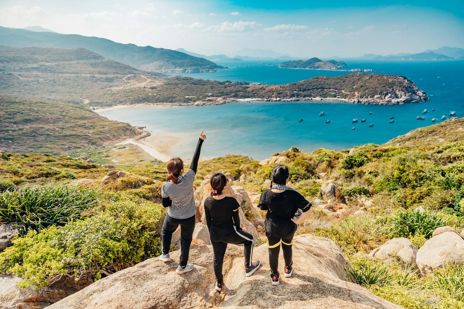 Three women standing together on a mountain ridge on a hiking trip, backpacks on, looking out over the valley