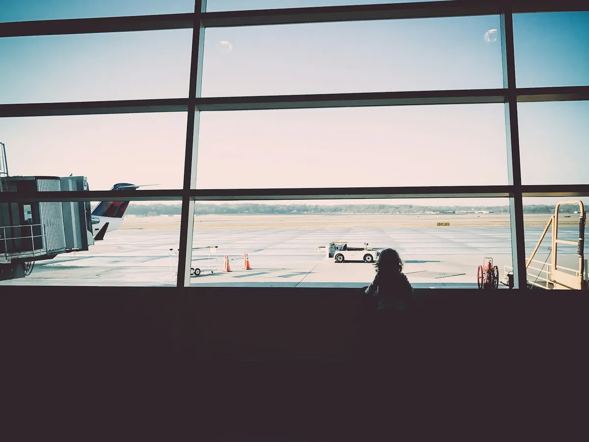 A silhouetted traveler looking out a large airport window at planes on the tarmac