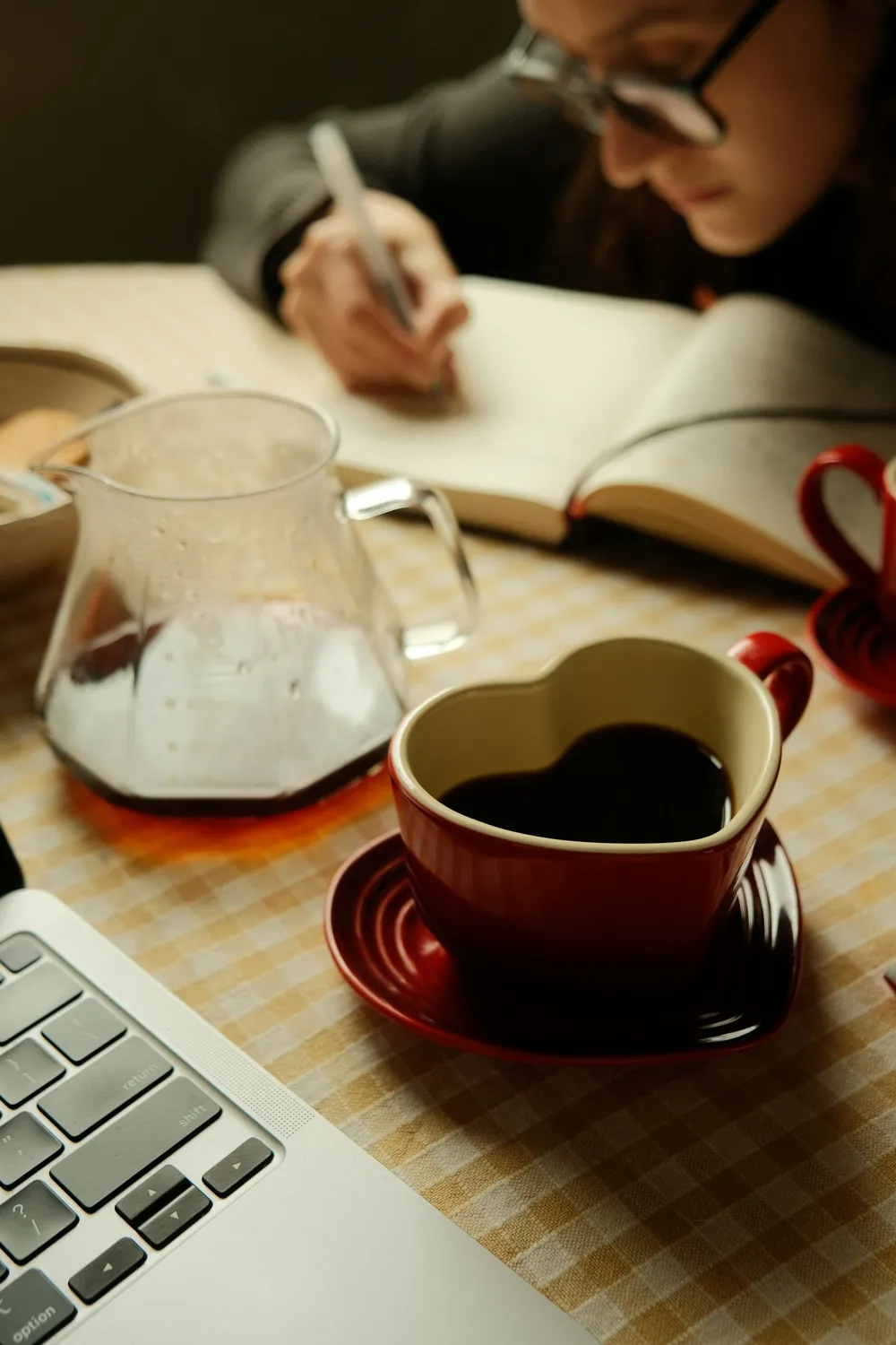 A woman writing in a notebook at a table with a laptop and a cup of coffee, planning a trip