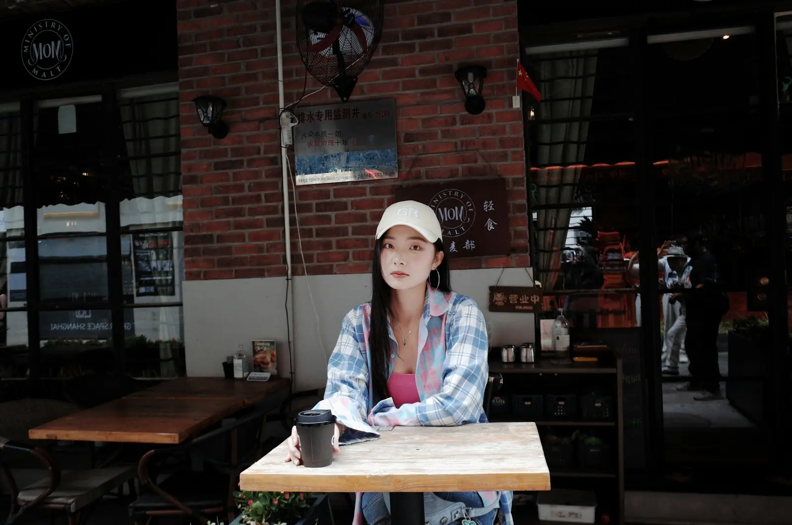 A woman sits by herself at an outdoor cafe table with a coffee, taking a quiet moment alone