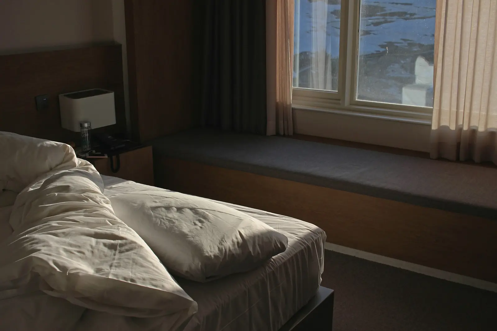 A tidy hotel room with a single bed, nightstand, and warm evening light through the window