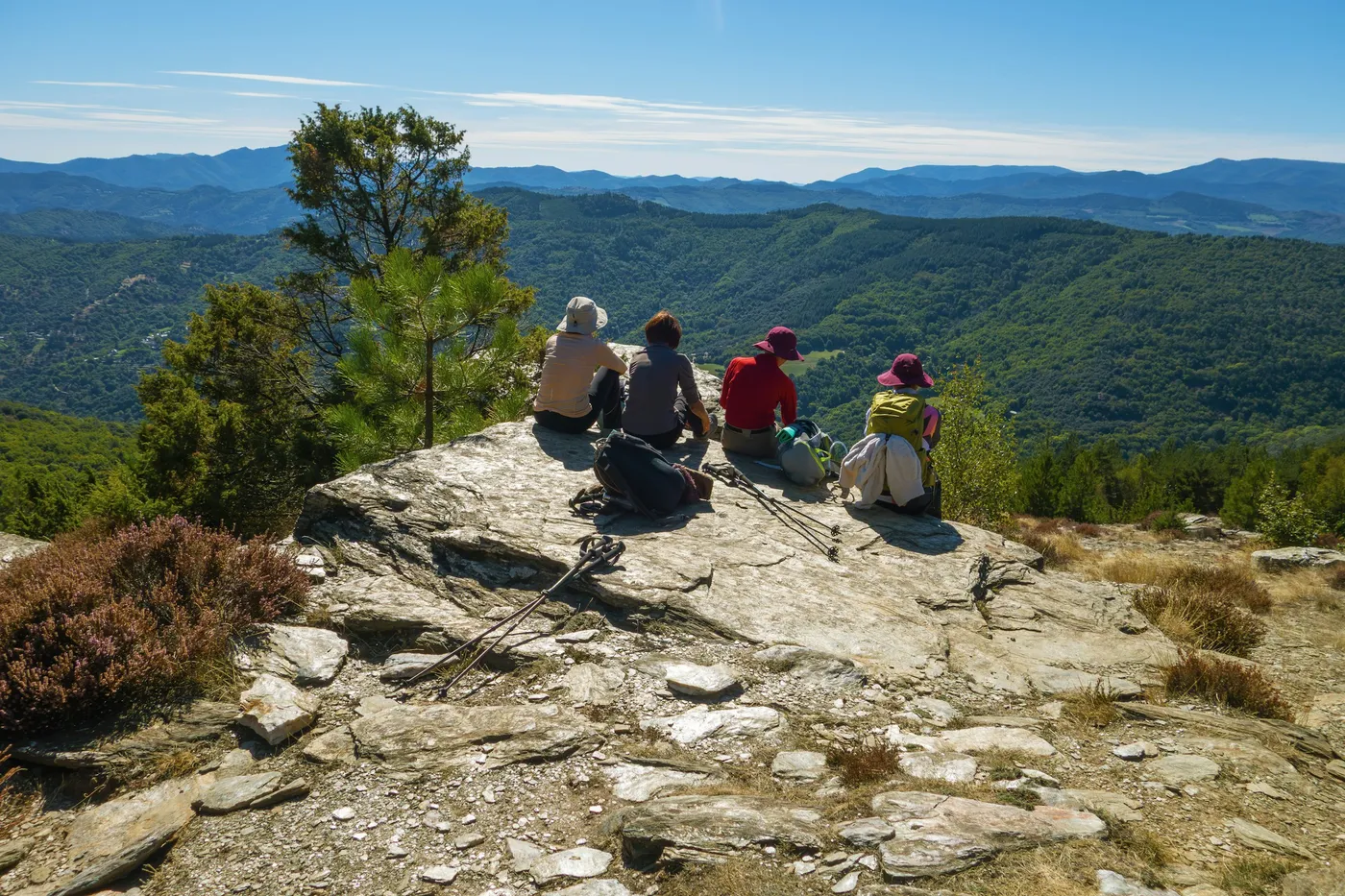 A small group of hikers resting together on a rocky viewpoint overlooking green hills